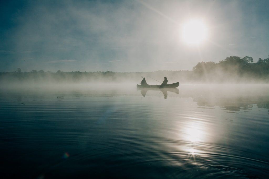 Tiedonhaku on kuin kalastamista. Kuvassa on kauempana järvellä tai merellä vene, jossa kaksi ihmistä. Taustalla paistaa aurinko.